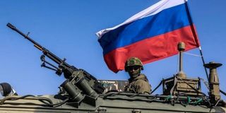 A Russian soldier atop an armored vehicle carrying Russian flag