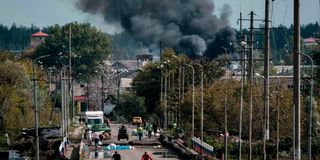 People cross a bridge over the Oskil River as smoke rises in city of Kupiansk