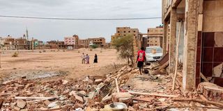 People walk near the rubble at a house that was hit by an artillery shell